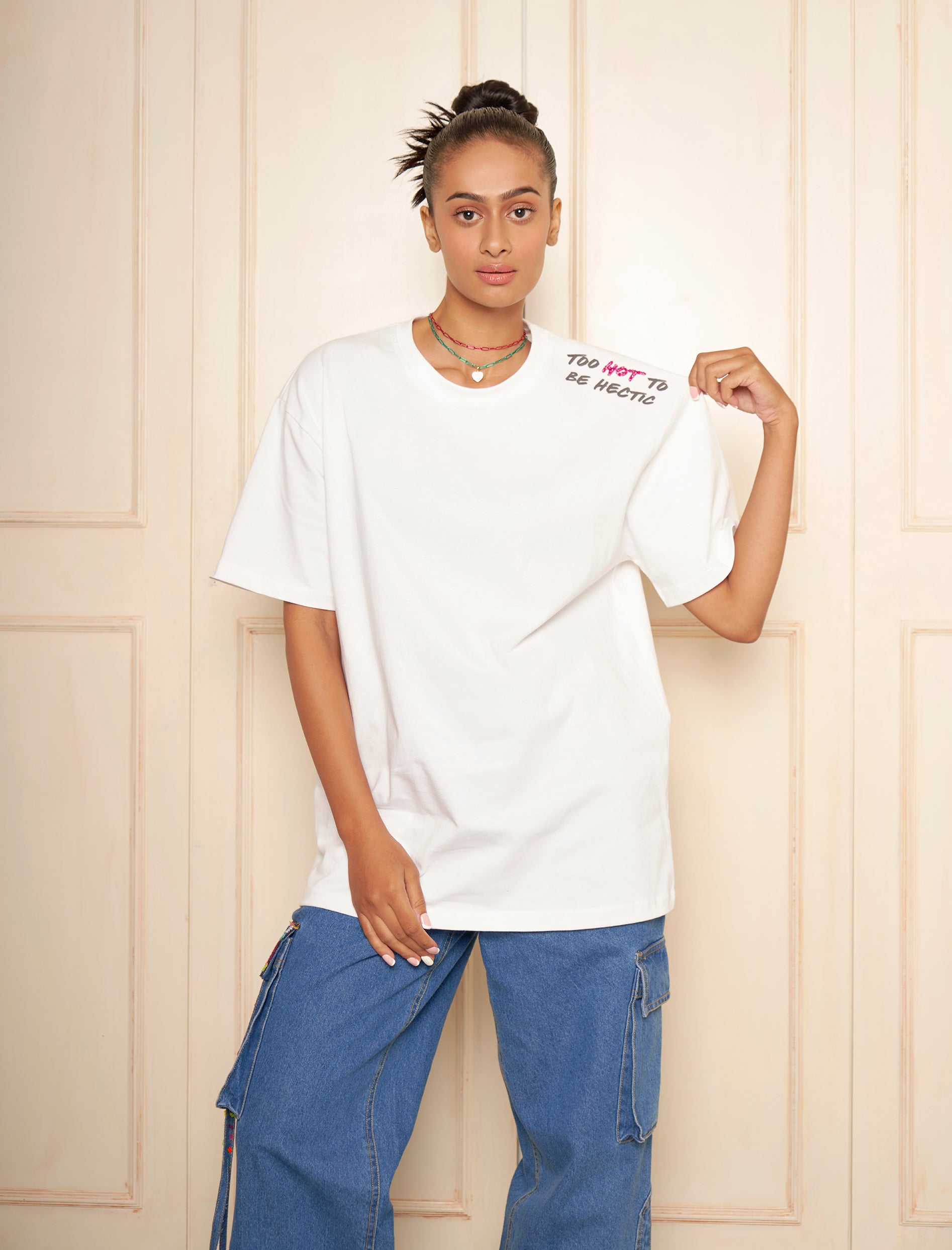 Wearing a white oversized t-shirt with embroidered text on the left shoulder, paired with blue jeans.