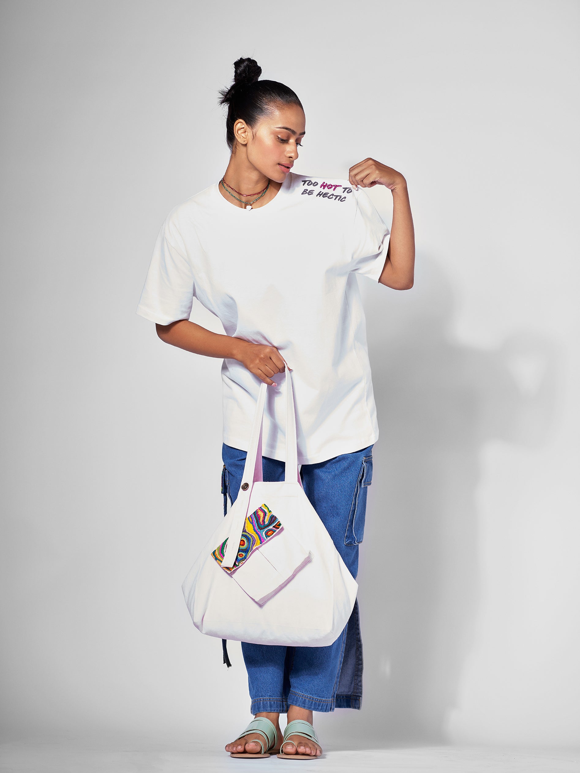 Wear a white oversized t-shirt with embroidered text on the left shoulder, paired with blue jeans.